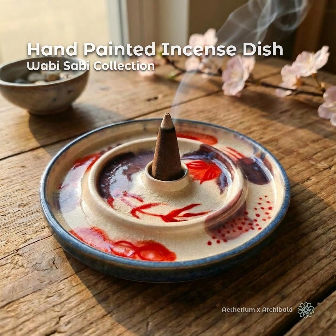 Hand-painted ceramic incense dish from the Wabi-Sabi Collection, shown on a rustic wooden table with a lit incense cone releasing soft smoke. The dish features a cream crackle glaze (kannyū-inspired) with abstract red and muted purple botanical brushwork, a raised central incense holder, and a blue-toned rim. Natural light and flowers create a calm, contemplative setting.