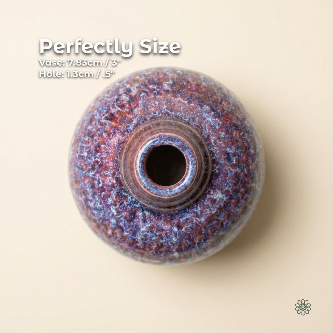 Top-down photograph of a handmade ceramic art vase centered on a light cream background. The vase has a rounded, spherical body with a small, circular opening at the center. The surface is covered in a reactive glaze with dense mottled textures in blue, violet, and rust tones. Around the opening, concentric glaze rings are visible. White text in the upper left reads “Perfectly Size,” followed by “Vase: 7.83 cm / 3 in” and “Hole: 1.3 cm / 0.5 in.” The aetherium logo in the bottom right.