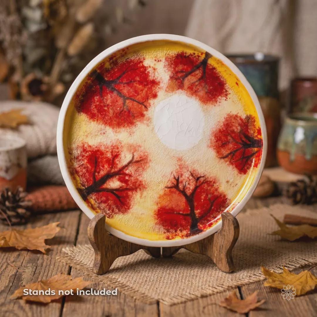 Hand-painted ceramic art plate displayed upright on a wooden stand on a rustic table. Features red autumn tree imagery, warm golden glaze tones, and a visible crackle finish. Wooden stand shown for display only and not included.