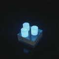 Three glow-in-the-dark toothpaste transfer adapters illuminated in low light on a clear acrylic block. The bright blue glow highlights nighttime visibility for campsite or travel use, showing how the adapters can be easily found in dark packs or tents.