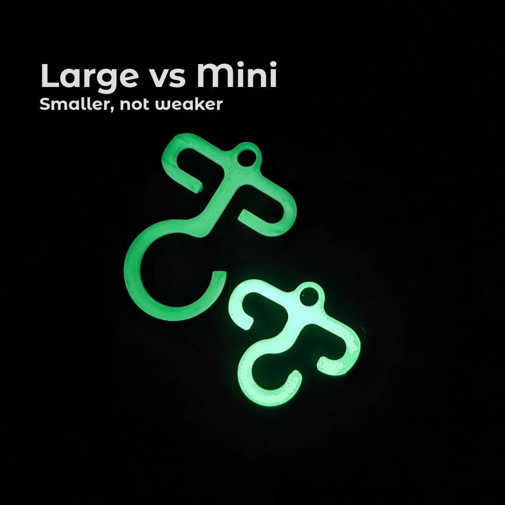 Side-by-side glow-in-the-dark paracord hooks, one full size and one mini. Black background highlights brightness and shape difference with on-screen text reading “Large vs Mini: Smaller, not weaker.” Designed to compare strength and portability for camping setups.
