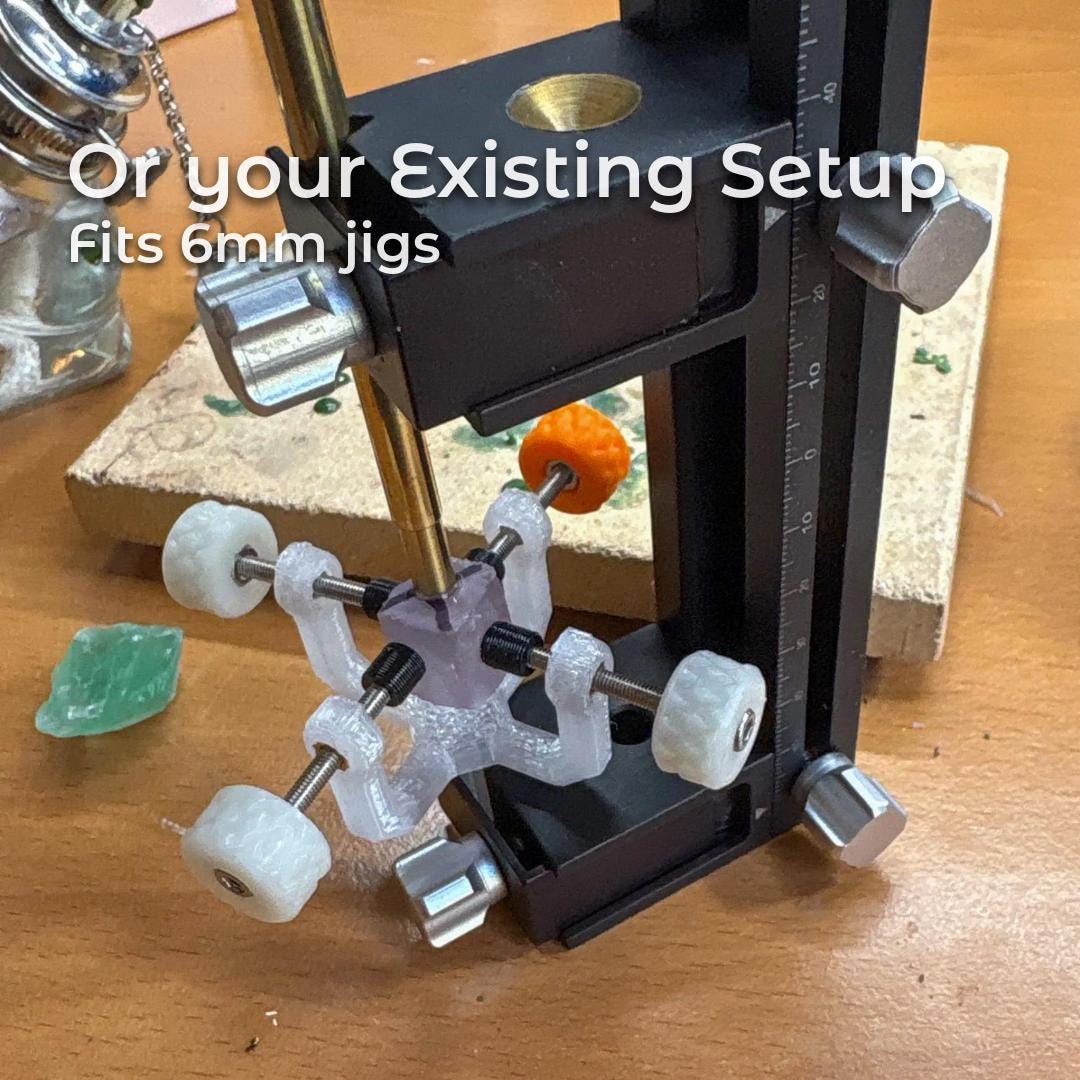 Text reads “Or your Existing Setup” and “Fits 6mm jigs.” The image shows the Gem Axis V3 stone alignment tool mounted inside an existing faceting machine mast. A translucent polycarbonate alignment body with four adjustable arms and knurled knobs holds a dop assembly, demonstrating compatibility with standard 6 mm jigs and quills in traditional faceting setups without modifying the machine.