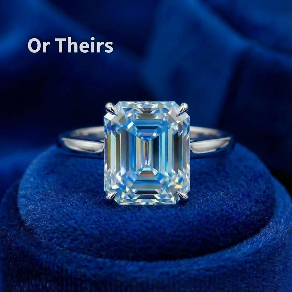 A blue emerald-cut moissanite mounted in a simple ring setting on blue velvet. The clean prongs frame the stone without obscuring the step facets. This image illustrates how the cut performs in a ring format, showing balanced proportions, centered table, and controlled light return. Setting shown for visualization only.