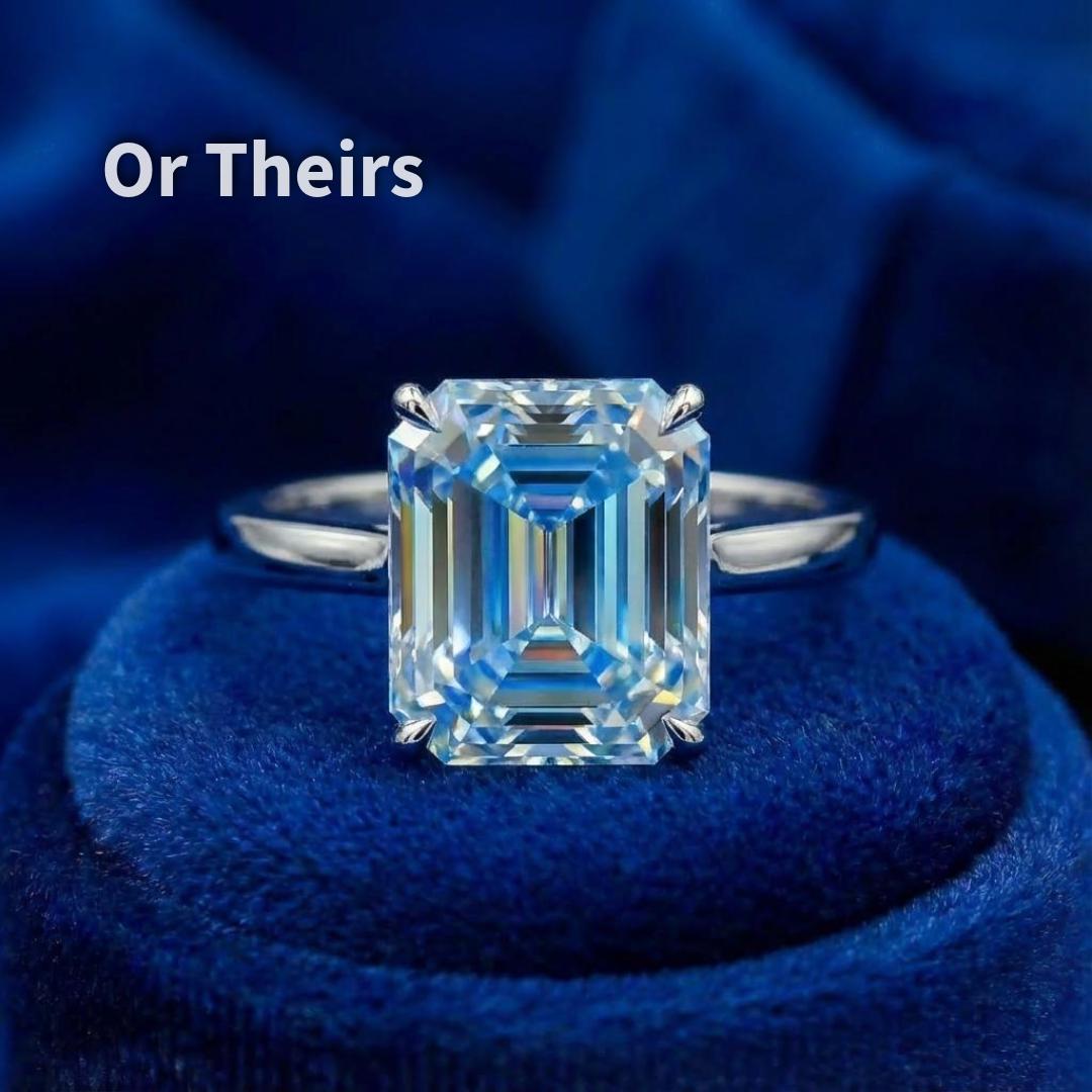 A blue emerald-cut moissanite mounted in a simple ring setting on blue velvet. The clean prongs frame the stone without obscuring the step facets. This image illustrates how the cut performs in a ring format, showing balanced proportions, centered table, and controlled light return. Setting shown for visualization only.