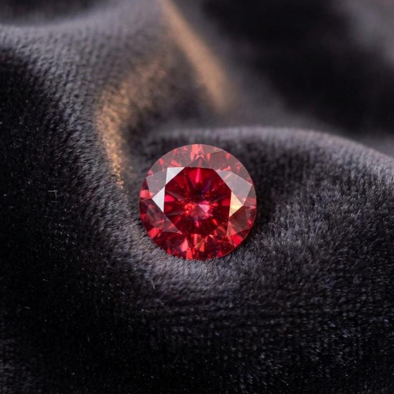 Loose ruby moissanite gemstone, 1 ct round cut with Russian-style brilliant faceting. Vivid red color with strong light return and crisp facet junctions. Shown unset to highlight optical performance, symmetry, and clarity. Ideal for jewelers, custom ring builds, or collectors sourcing premium lab-grown stones.