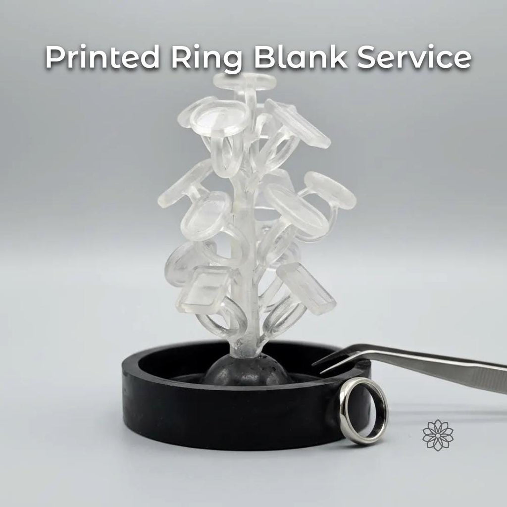 Clear PolyCast PVB 3D printed ring blanks arranged on a sprue tree, standing upright in a black casting base. Multiple oval, round, and rectangular ring blank shapes are visible, showing smooth surfaces and uniform wall thickness. A finished silver ring rests beside the base, suggesting the transition from printed casting pattern to completed jewelry. Neutral studio background with soft lighting emphasizes material clarity and form.