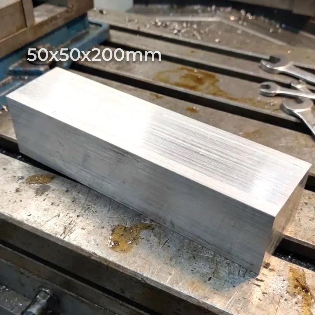 A rectangular 200 mm aluminum 6160-T6 bar blank positioned on a metal mill bed, with visible cutter marks and shop tooling in the background. Raw stock for machining, milling fixtures, jigs, and precision components.