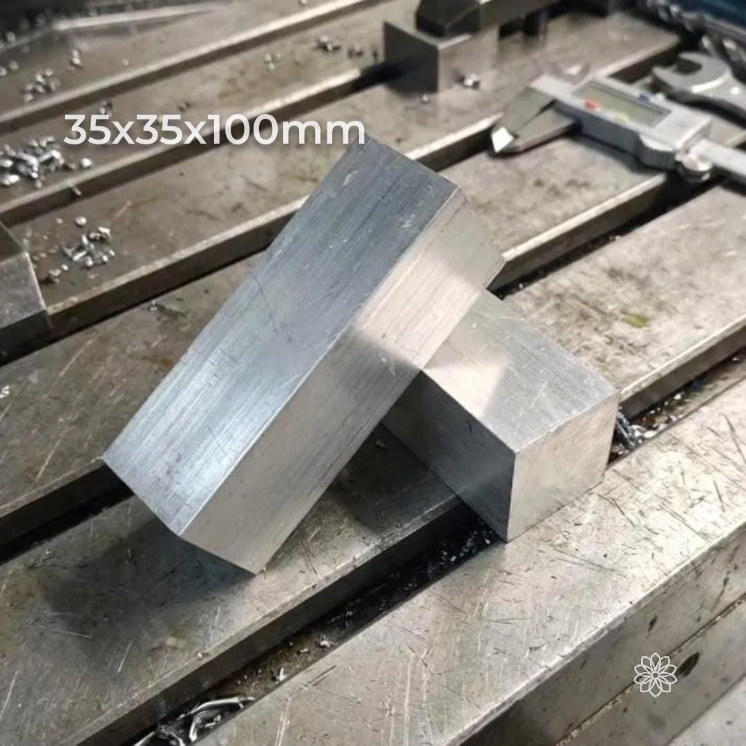 Two 35×35×100 mm 6061-T6 aluminum bar stock pieces resting on a CNC mill table with chips scattered around. Raw aluminum blocks ready for machining drone frames, small engine parts, jigs, fixtures, and precision prototypes. Clean edges and consistent billet finish visible.