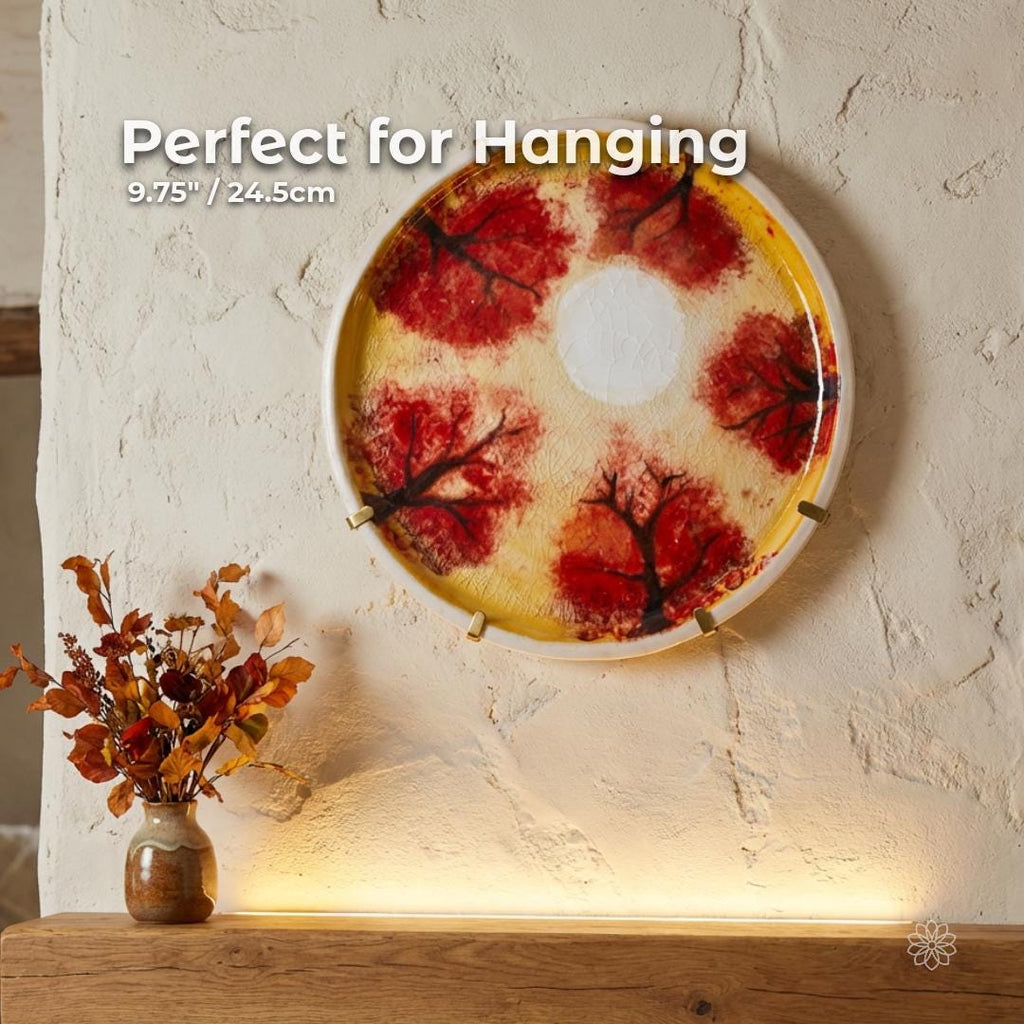 Round hand-painted ceramic art plate designed for wall hanging, measuring approximately 9.75 inches or 24.5 cm in diameter. Displays red foliage motifs, warm yellow tones, and a kannyū crackle glaze surface with metal wall hangers visible.