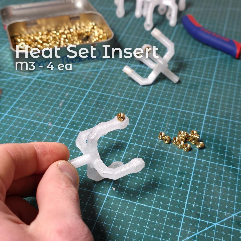 Close-up of a printed polycarbonate Gem Axis V3 arm with brass heat-set inserts installed, shown alongside loose inserts and tools. The image documents the reinforced threaded interfaces used in the alignment tool to ensure durability and repeatable precision adjustments.
