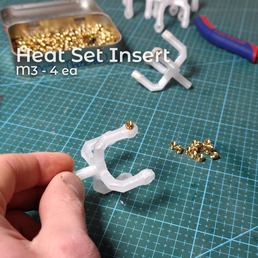 Close-up of a printed polycarbonate Gem Axis V3 arm with brass heat-set inserts installed, shown alongside loose inserts and tools. The image documents the reinforced threaded interfaces used in the alignment tool to ensure durability and repeatable precision adjustments.