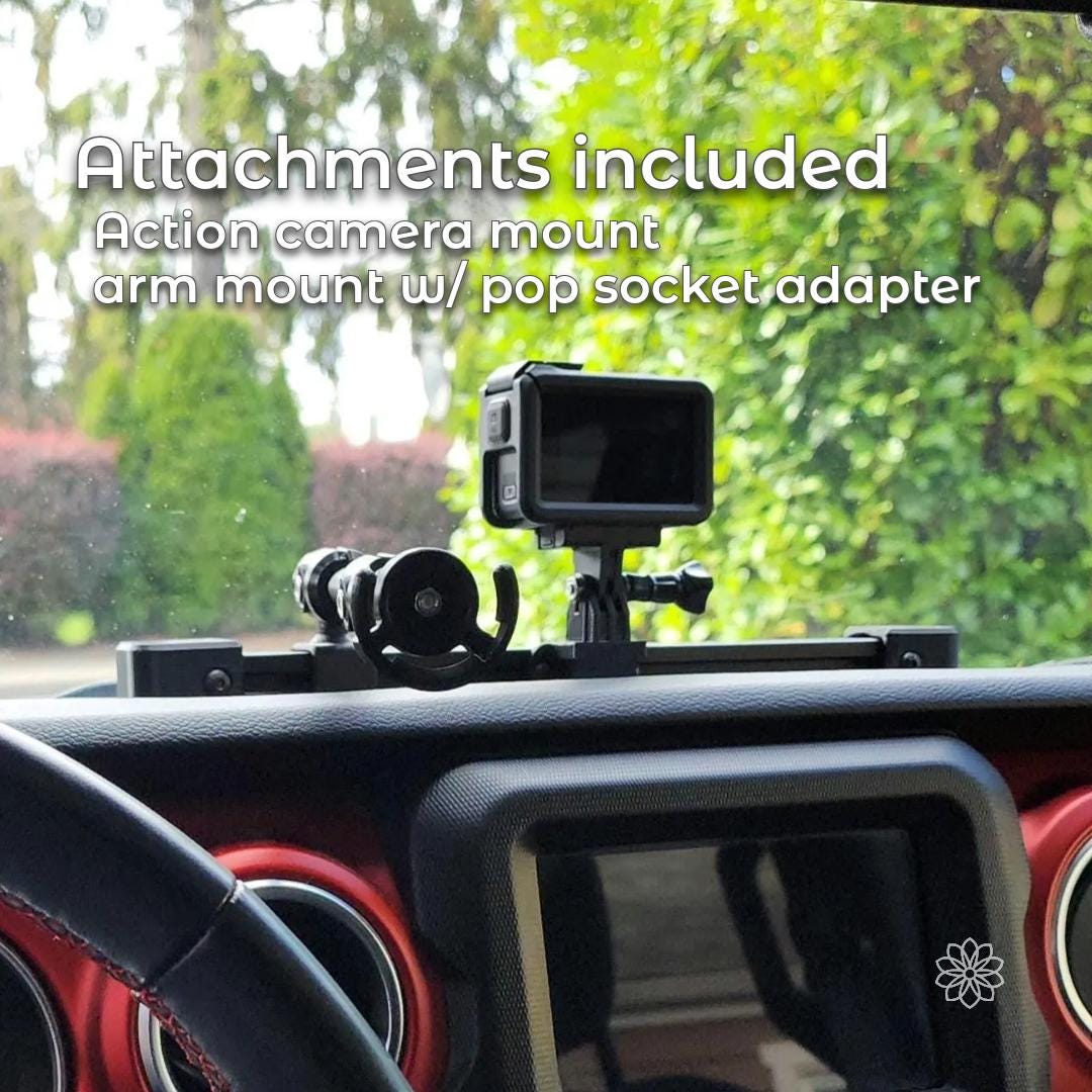 Jeep dash accessory rail shown with included attachments mounted to the aluminum extrusion, including an action camera mount and an adjustable arm with PopSocket-compatible phone holder. The system is installed across the dashboard and demonstrates multiple mounting positions along the rail for phones and cameras.