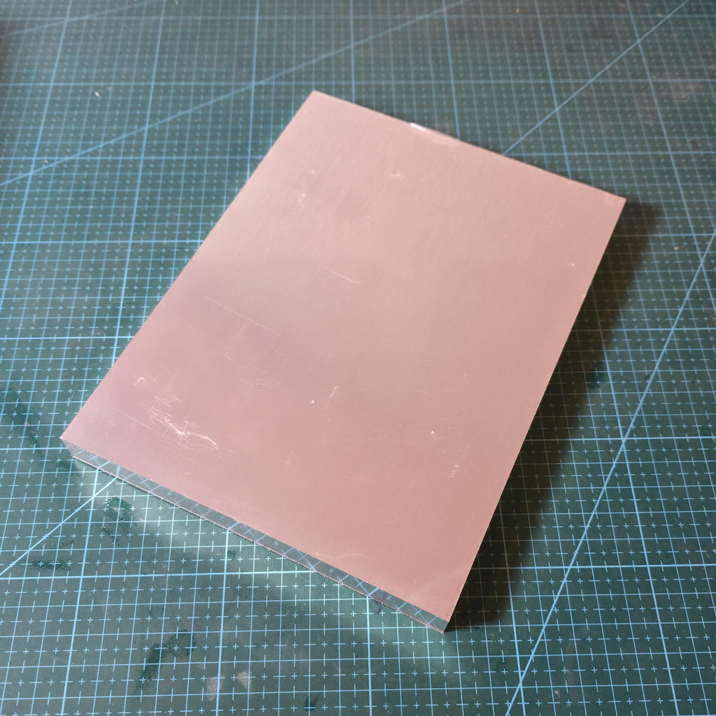 6061 Aluminum Plate CNC sheet stock lying flat on a blue gridded cutting mat, large rectangular plate with visible brushed finish and light surface marks, ready for CNC milling, router work, and fixture or jig making.