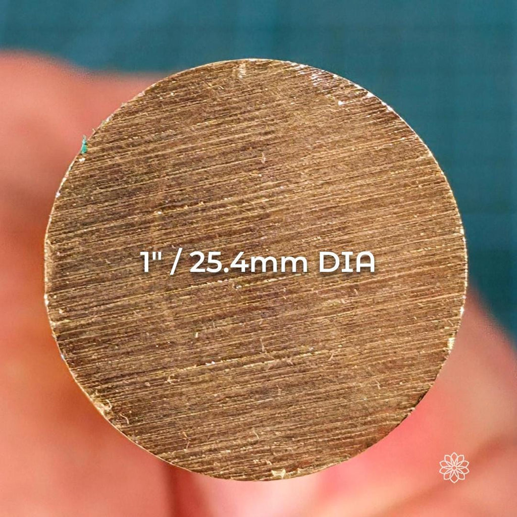End-on close-up view of a brass round rod showing a flat, circular cross-section with visible saw cut marks. Overlay text indicates a diameter of 1 inch or 25.4 millimeters. The image emphasizes diameter accuracy, solid stock consistency, and suitability for CNC lathe turning and precision machining.