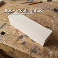 “A rectangular epoxy tooling block sitting on a woodworking bench. The block has a smooth, uniform surface and sharp machine-cut edges, showing its use as a rigid fixture material for CNC machining, prototyping, and precision modeling. Tools and wood shavings surround the block in a workshop setting. Text highlighting that this is ideal for CNC practice cuts”