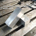 50×50×50 mm 6061-T6 aluminum bar stock block on a CNC mill bed, surrounded by metal chips. Matte silver surface with saw marks and sharp edges. Ideal raw material for CNC machining, milling, drilling, prototyping, fixturing, and precision metalworking projects.
