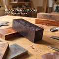 Black Delrin square block CNC machining stock resting on a wooden workbench, surrounded by hand tools and sanding blocks. The solid acetal plastic block shows raw machined faces and surface marks typical of cut stock, highlighting its use for CNC fixtures, jigs, prototyping, and functional machining applications in a maker or small-shop environment.