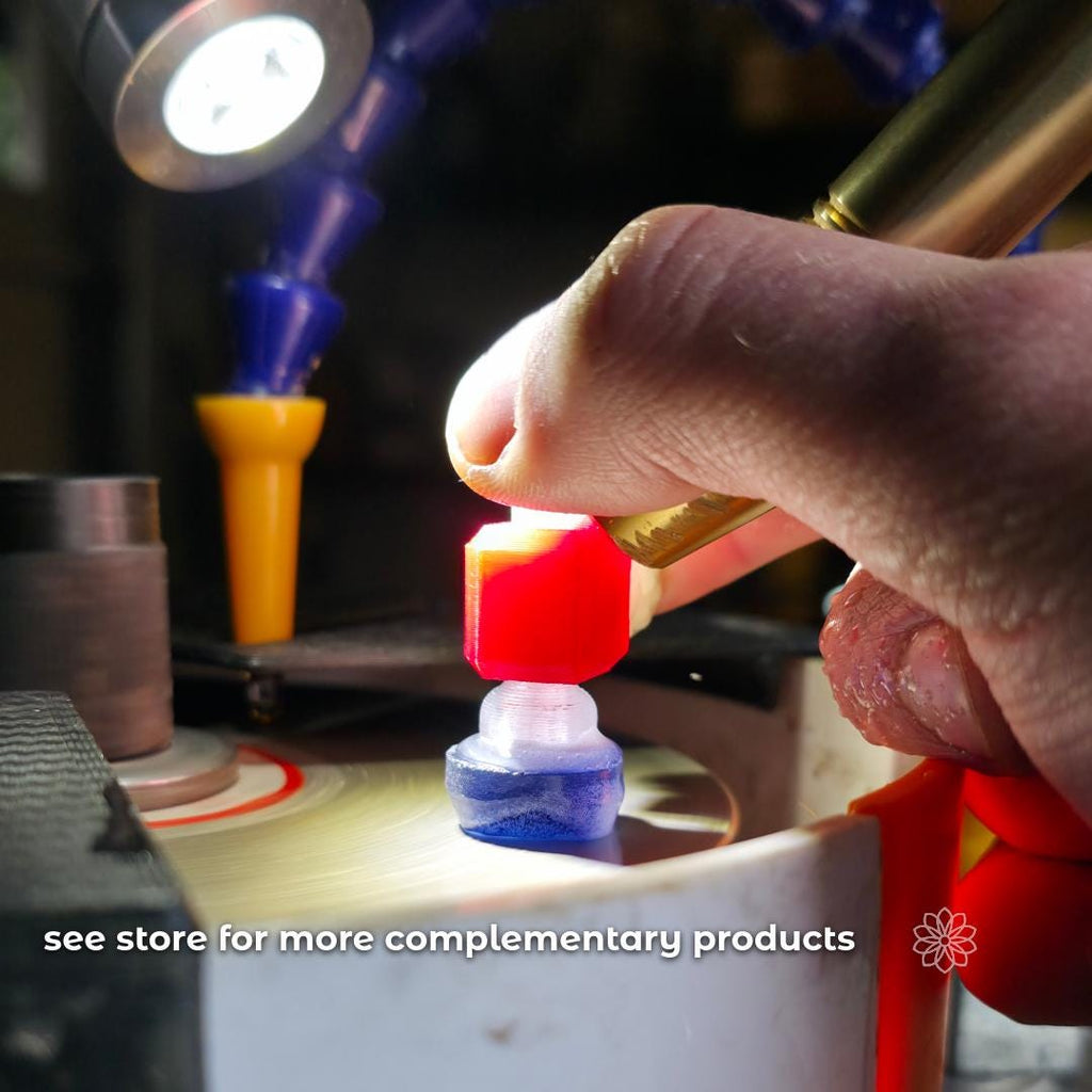 In-use workshop photo of a hand holding a dop stick against a spinning lap on a Vevor faceting machine, with water flowing and the upgraded water baffle visible around the basin edge. On-image text reads “see store for more complementary products.” The scene shows real cutting conditions with task lighting and controlled water flow.