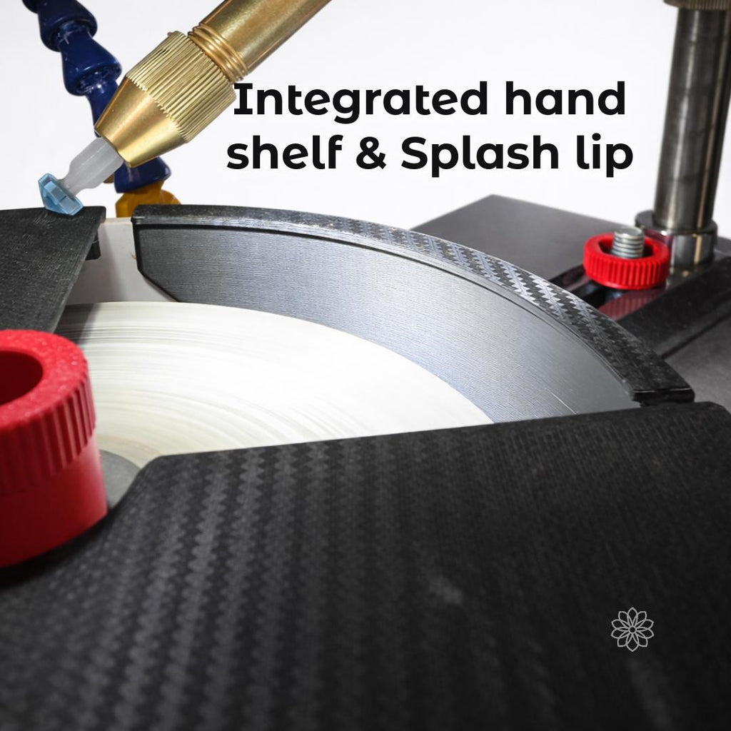 Close-up view of a faceting machine basin featuring a curved water baffle shield with an integrated hand shelf and internal splash lip. On-image text reads “Integrated hand shelf & Splash lip.” The image shows a gemstone approaching the lap, emphasizing improved hand support, reduced fatigue, and better water control during faceting.