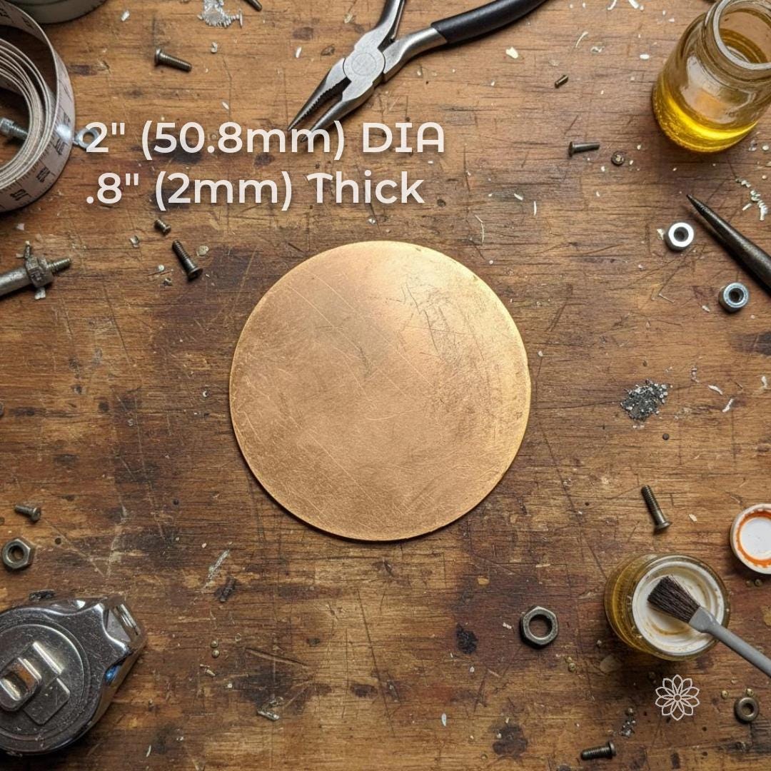 “A single round brass disk centered on a worn workbench, surrounded by hand tools, screws, and a small jar with a brush. The disk surface shows natural scratches from cutting and handling, representing a raw brass blank ready for CNC machining, stamping, or jewelry engraving.” Size specifications in text read 2" (50.8mm) dia, .8" (2mm) thickj