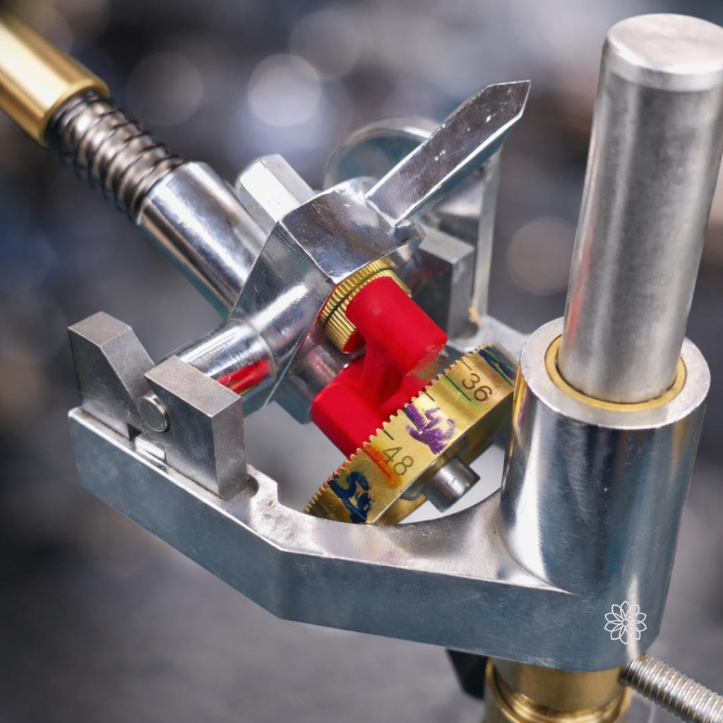 Detailed view of a gemstone faceting machine head showing the red Free Spin Adapter engaged against the brass index gear. The adapter pulls the index spring back to release the gear teeth, allowing the quill assembly to rotate freely for preforming stones.