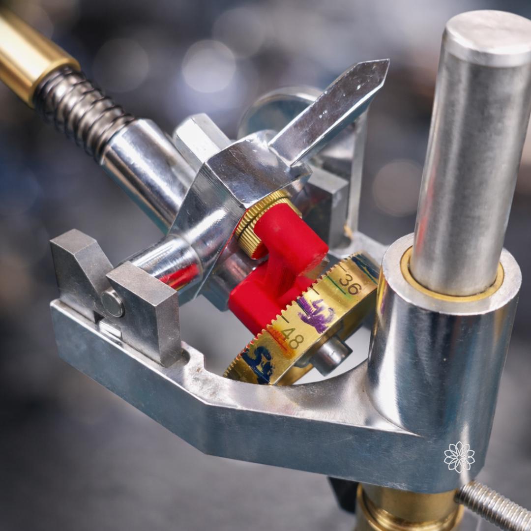 Detailed view of a gemstone faceting machine head showing the red Free Spin Adapter engaged against the brass index gear. The adapter pulls the index spring back to release the gear teeth, allowing the quill assembly to rotate freely for preforming stones.