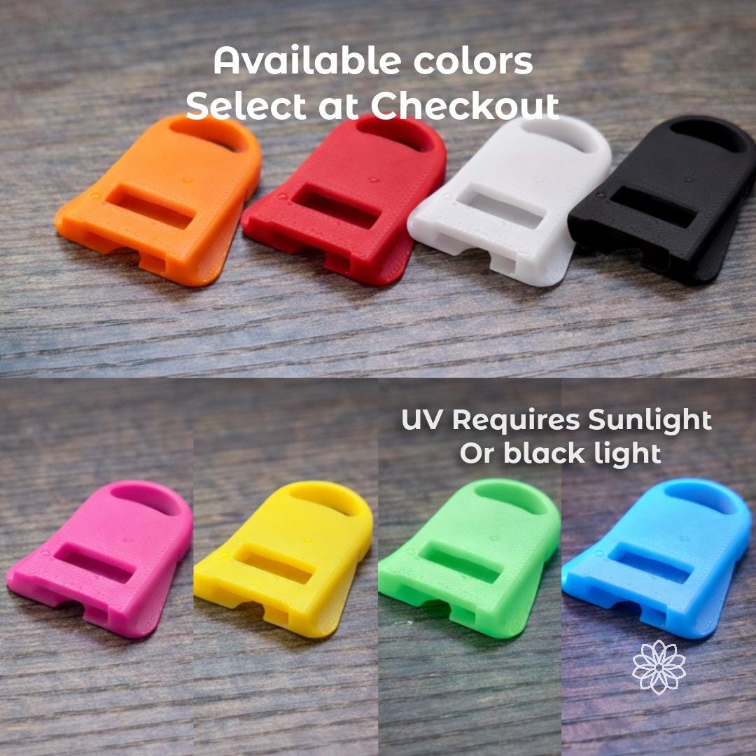 Multiple Aetherium Can Guard camping drink tools displayed on a wooden surface in different color options including orange, red, white, black, pink, yellow, green, and blue. These compact can opener and drink shield accessories attach to beverage cans to assist opening pull tabs and protect drinks from insects while camping, hiking, or relaxing outdoors. Overlay text indicates available colors and UV variants.