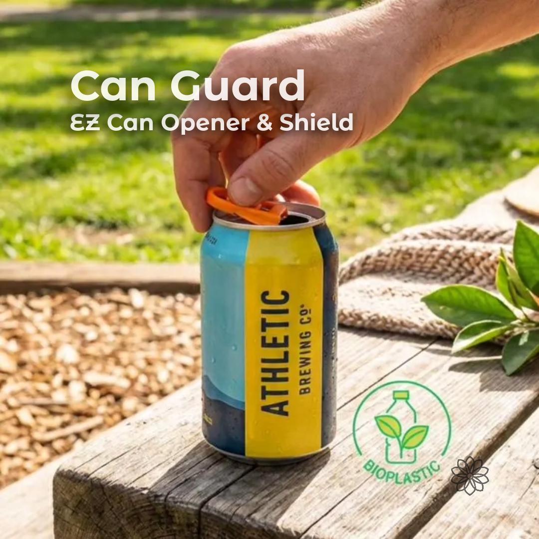 Hand opening a beverage can using the Aetherium Can Guard EZ can opener and drink shield attached to an aluminum drink can on a wooden picnic table outdoors. The orange camping can tool lifts the pull tab without finger strain and rotates to cover the opening, helping keep bugs and debris out during camping, picnics, or outdoor gatherings. Overlay text reads “Can Guard – EZ Can Opener & Shield” with a bioplastic material icon.