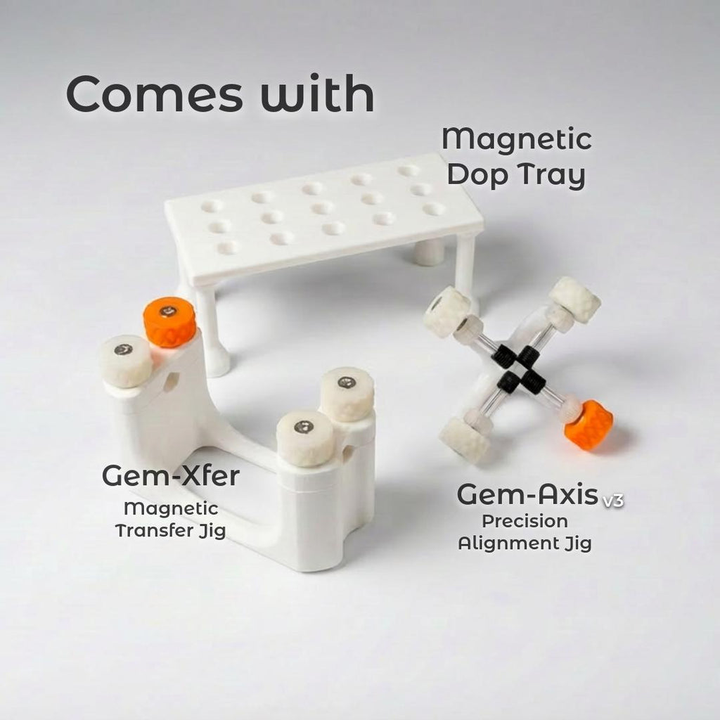 Gem Cutting Essentials Tool Kit by Aetherium Innovations displayed on a bright surface. The set includes a white Gem Xfer epoxy transfer jig with orange and white knurled knobs, a Gem Axis v3 alignment jig with white adjustment wheels and orange handle, and a white magnetic dop stick tray with 15 holes for holding dops. Clean studio lighting highlights the professional, precision-engineered design for lapidaries of all skill levels.
