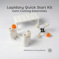 "Components of the Lapidary Gem Cutting & Polishing Kit by Aetherium Innovations. labeled on a wood surface: the Gem Xfer, Gem Axis, and Dop Stick Tray. Each tool features 3D-printed polymer parts with textured knobs for grip. Text overlays identify each part, showing the organized and educational layout ideal for gemstone work."