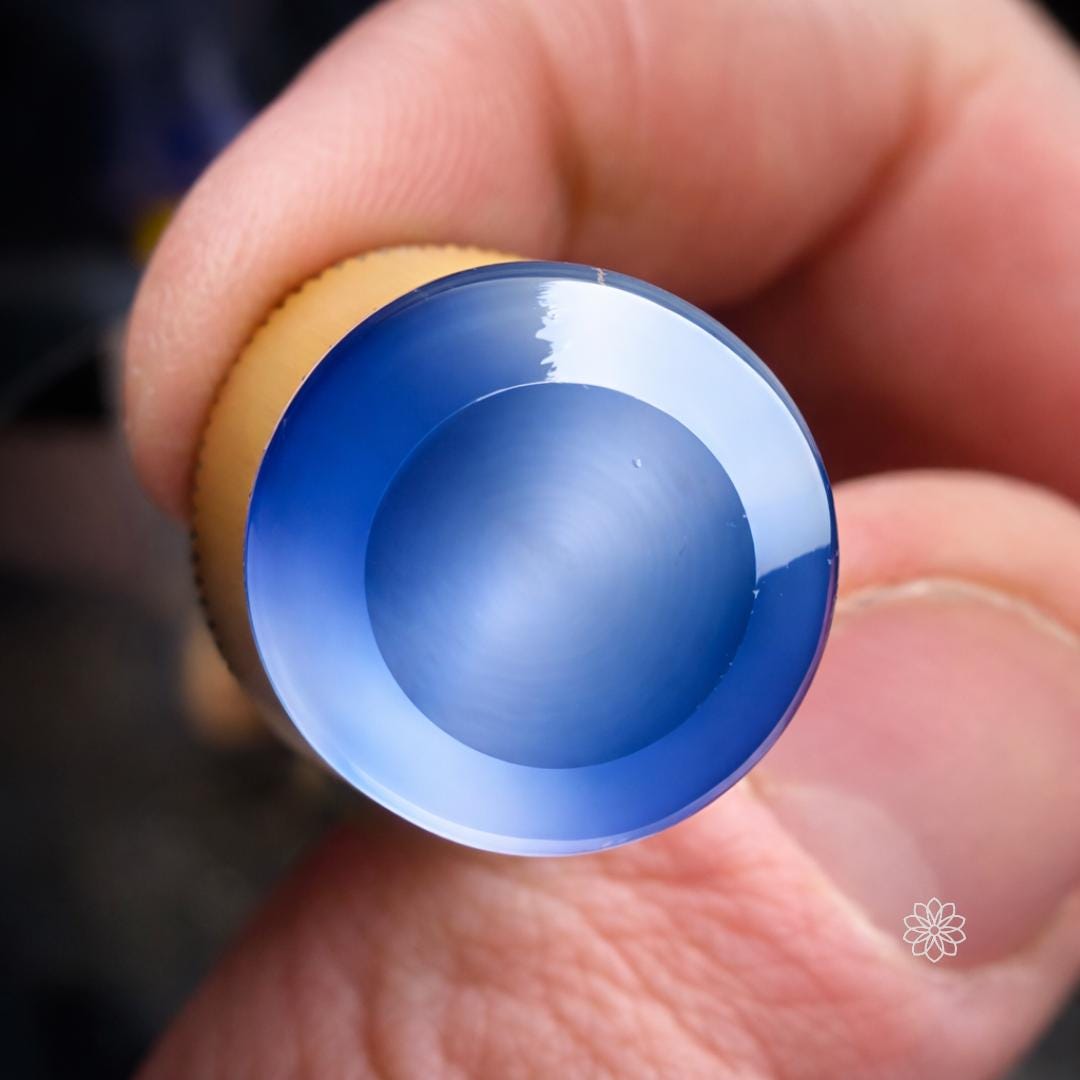 Close-up of a polished blue sapphire gemstone table surface reflecting blue light after being cut flat on a faceting machine. The smooth circular polish demonstrates the type of flat table or window surface achieved using a precision tabling adapter and diamond lap during lapidary faceting work.
