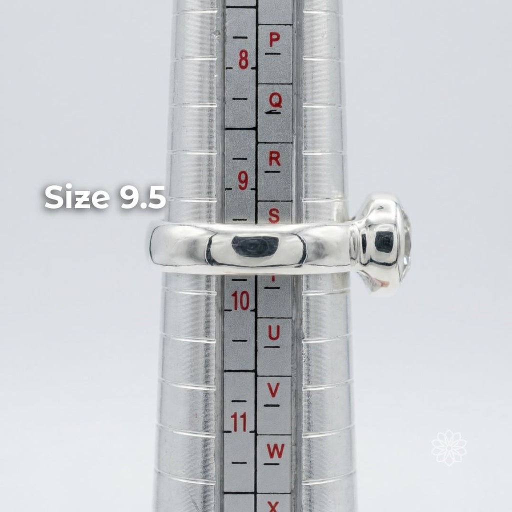 Side profile of a sterling silver bezel-set moissanite ring on a metal ring mandrel showing the band shape, low setting height, and scale. The ring is displayed at size 9.5. Visible text says “Size 9.5.”