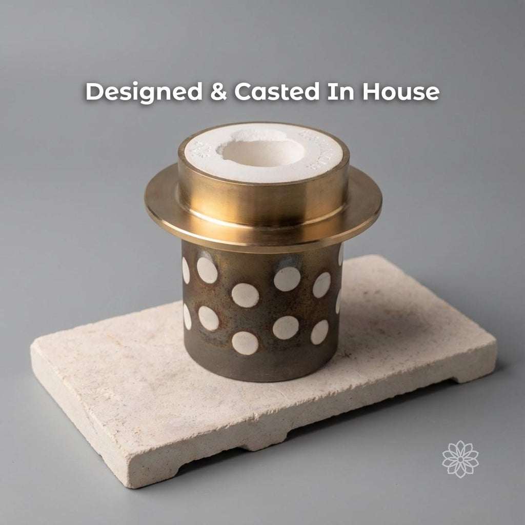 Perforated metal casting flask with a white investment core sits on a ceramic block against a plain background, representing the in-house casting process used to make Aetherium jewelry. Visible text says “Designed & Casted In House.”