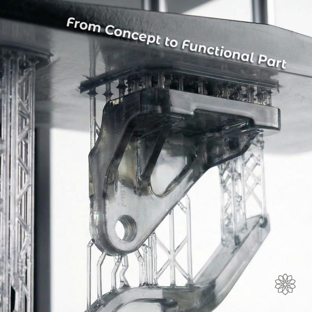 Clear resin printed mechanical component with internal supports and complex geometry, attached to a build plate during printing. Transparent photopolymer material reveals internal structure, demonstrating capability for functional prototypes and precision parts with intricate features and tight tolerances.
