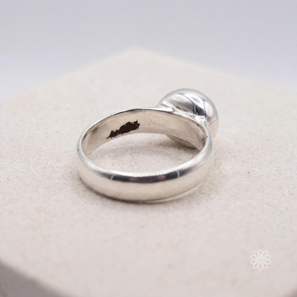 Back view of a sterling silver bezel-set moissanite ring resting on a light surface, showing the smooth polished band, underside of the bezel setting, and handmade interior finish with makers marks. This angle highlights the ring’s low profile and solid silver construction.