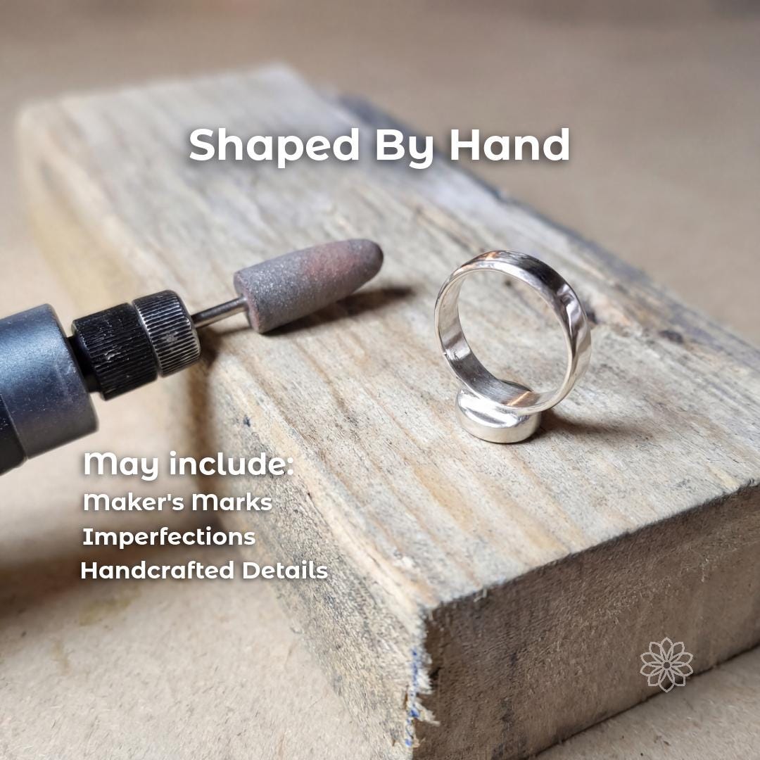 Sterling silver ring setting being hand shaped and refined on a wood bench beside a rotary polishing tool. The image shows the handcrafted finishing stage before stone setting. Visible text says “Shaped By Hand” and “may include: Maker’s Marks Imperfections Handcrafted Details.”