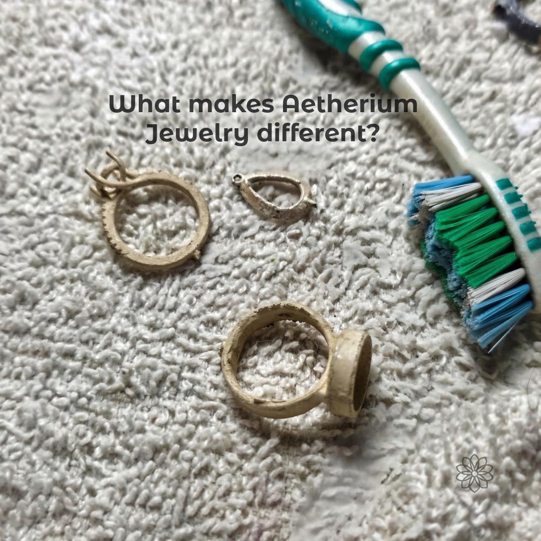 Jewelry work-in-progress components rest on a textured towel beside a toothbrush, including unfinished ring settings and cast metal parts used in the making process. This image supports the handmade workshop side of Aetherium jewelry. Visible text says “What makes Aetherium Jewelry different?”