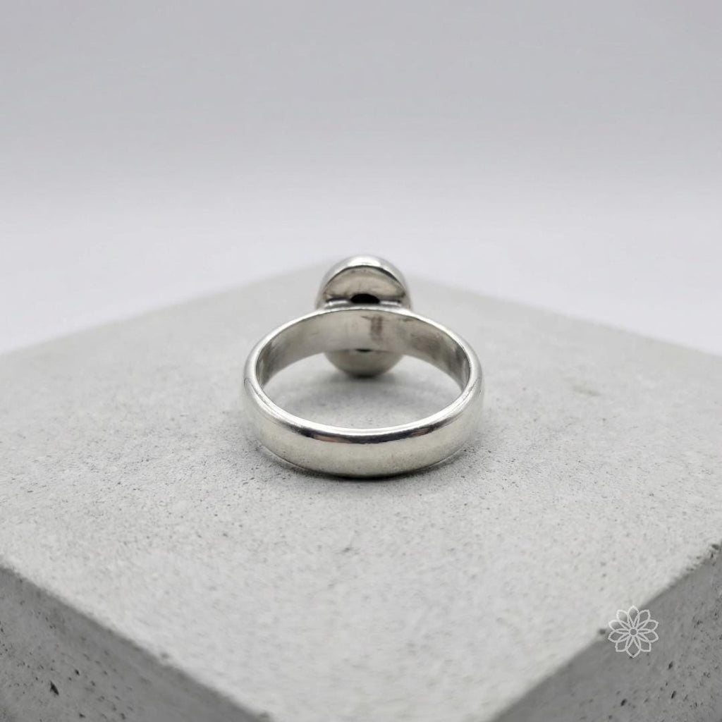 Back view of a sterling silver bezel-set sapphire ring showing the inside of the band with maker's marks and enclosed setting structure. The image highlights the low profile and solid construction of the ring.