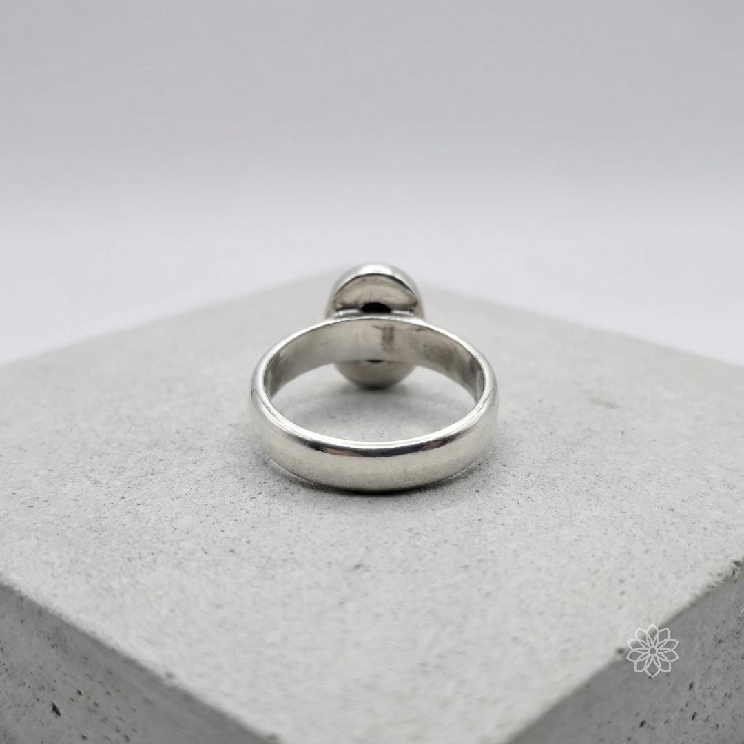 Back view of a sterling silver bezel-set sapphire ring showing the inside of the band with maker's marks and enclosed setting structure. The image highlights the low profile and solid construction of the ring.
