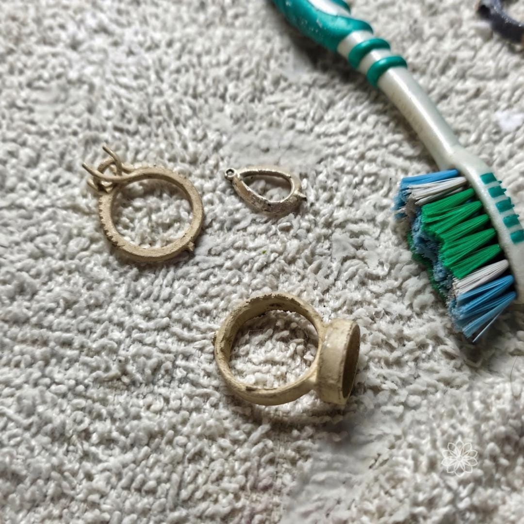 Raw ring components and casting remnants on a work surface next to a brush