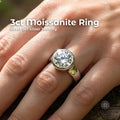 Hand wearing a 3ct moissanite ring in sterling silver bezel setting, photographed outdoors on natural wood surface. Brilliant round cut stone reflects high sparkle and fire in sunlight. Polished silver band with modern low profile design, shown on finger for scale and real-world appearance.