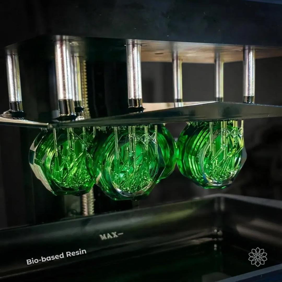 Green translucent resin parts suspended in a printing chamber, showing multiple small components produced in a single batch. Demonstrates batch production of detailed parts using bio-based resin, highlighting efficiency within small-format build constraints and consistent high-detail output.