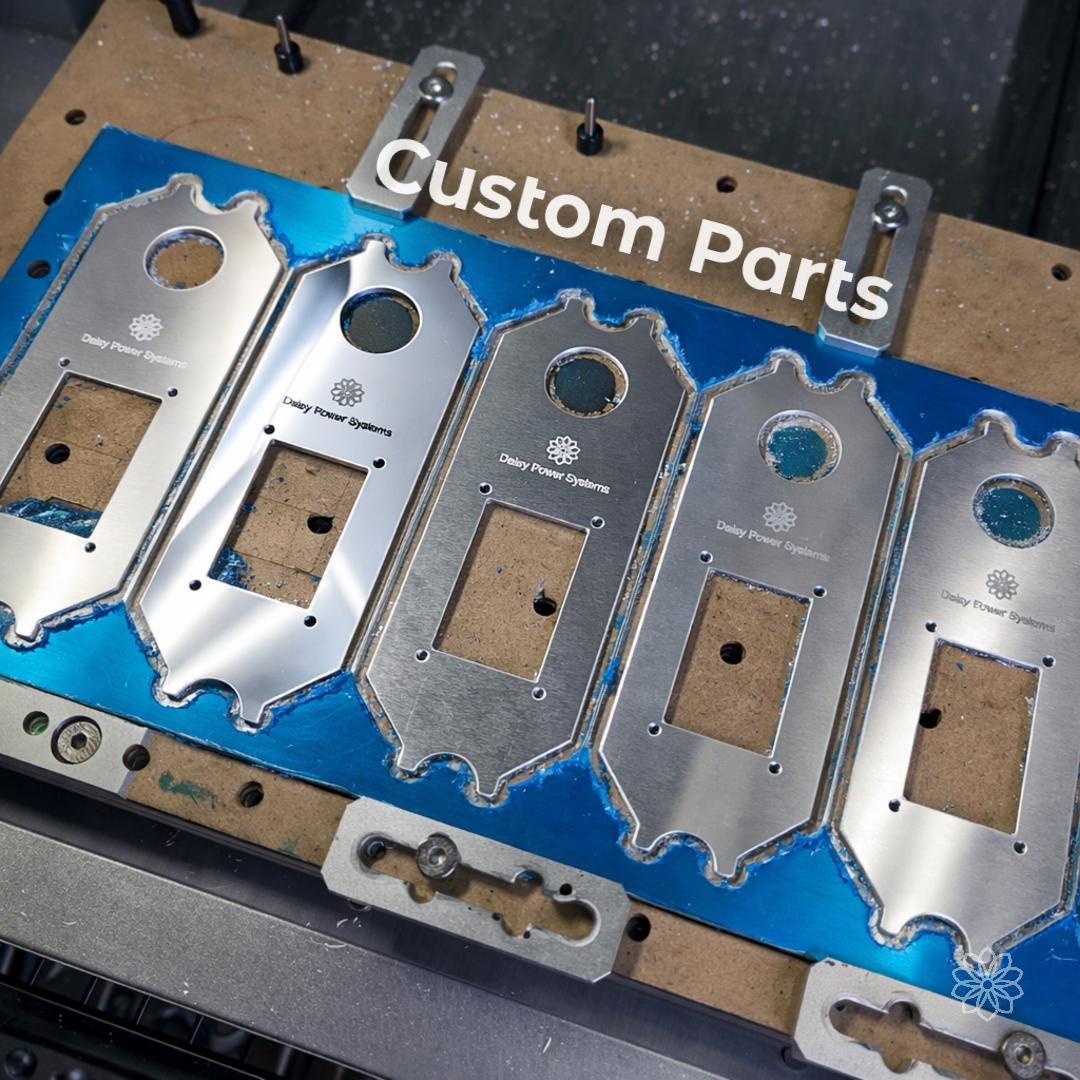Batch of machined aluminum plates mounted on CNC bed with consistent cut quality and repeatable geometry. Overlay text reads “Custom Parts.” Clean edges, uniform hole placement, and identical profiles demonstrate small batch production, fixture-based machining, and repeatability for functional components and product manufacturing.