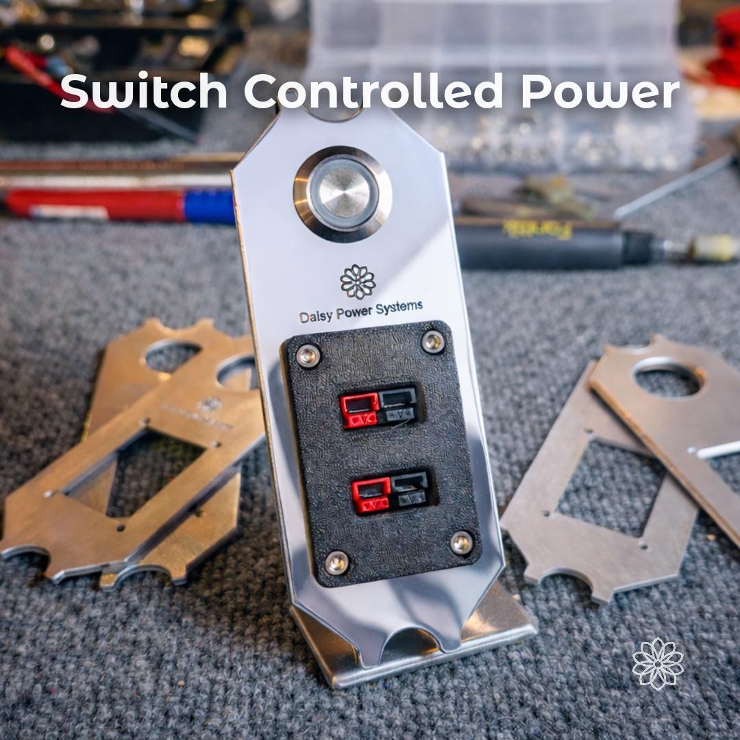 Text reads "Switch Controlled Power." Daisy Power Systems aluminum DC panel shown on a workshop surface with two round push