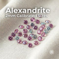 2mm round cut lab-grown alexandrite gemstones arranged on light fabric background. Stones show vivid pink and soft lavender tones with precise faceting. White overlay text in upper left reads “Alexandrite 2mm Round Cut.” Small calibrated accent stones for jewelry making, pavé, halo, and fine detail work requiring consistent sizing.