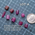 Lot A of natural pink Madagascar ruby and sapphire rough shown on a grid mat beside a dime for scale. Text lists average length 6.5mm, average width 6.3mm, and lot size 4.6 grams or 23 carats. The parcel shows varied pink corundum pieces for cabbing, small jewelry stones, carving, and exploratory cutting.