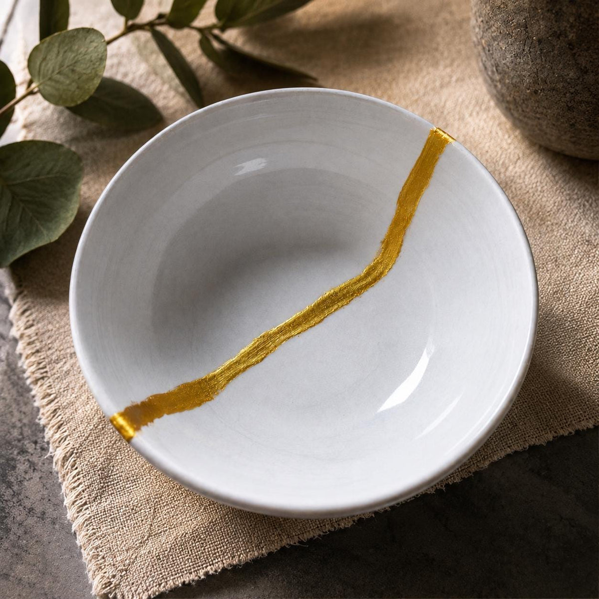 White ceramic bowl repaired using the Kintsugi technique with a metallic gold seam running across the surface. Gold mica powder pigment used to create decorative repair lines, Wabi-Sabi inspired restoration, ceramic repair art, gold resin accents, and traditional Japanese-inspired Kintsugi projects that celebrate imperfections through visible craftsmanship and metallic contrast.