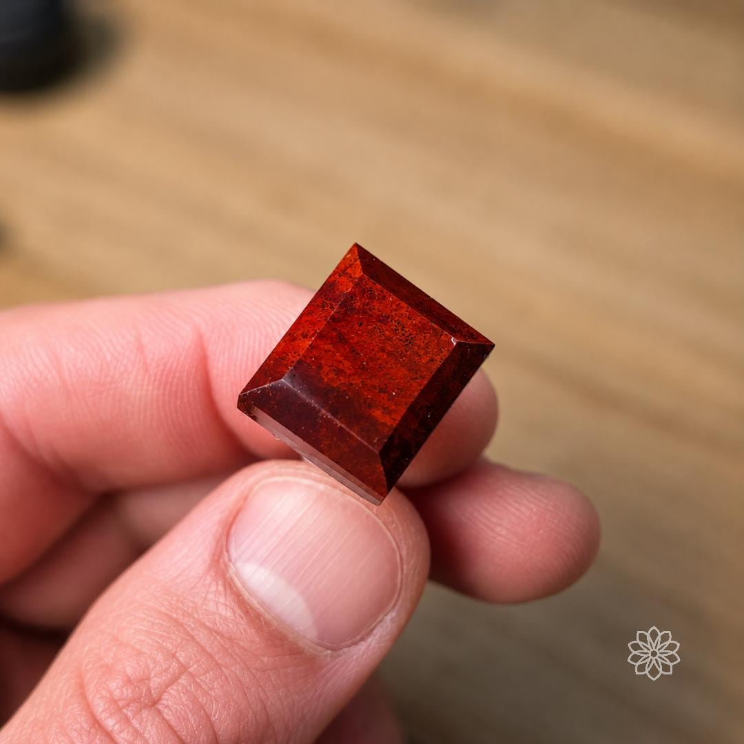 Hand holding a precision preformed square red gemstone with polished bevels