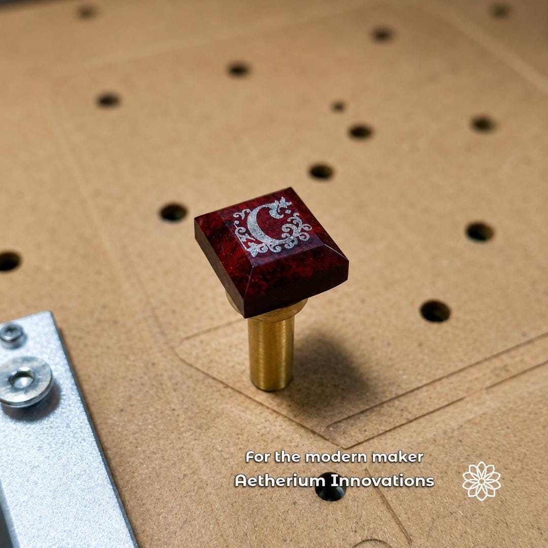 Engraved red gemstone mounted on a brass dop stick on a CNC work surface. Example of a modern maker workflow using lapidary tools for gemstone engraving, jewelry making, stone finishing, polishing, and precision craft production.