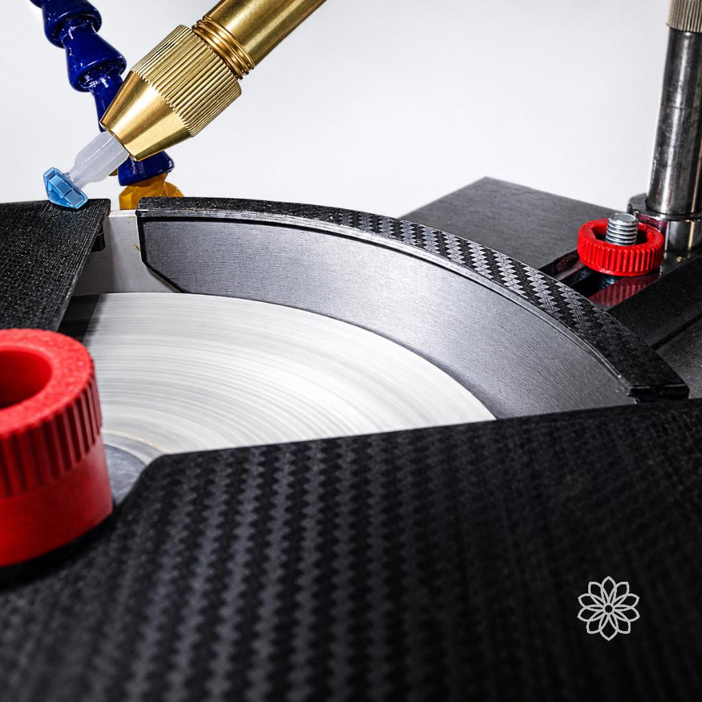 Close-up of black textured lap cover and side baffle around a spinning faceting lap with water nozzle and red thumb screws. VEVOR faceting machine accessory for splash reduction, lapidary water control, gemstone cutting, and polishing.